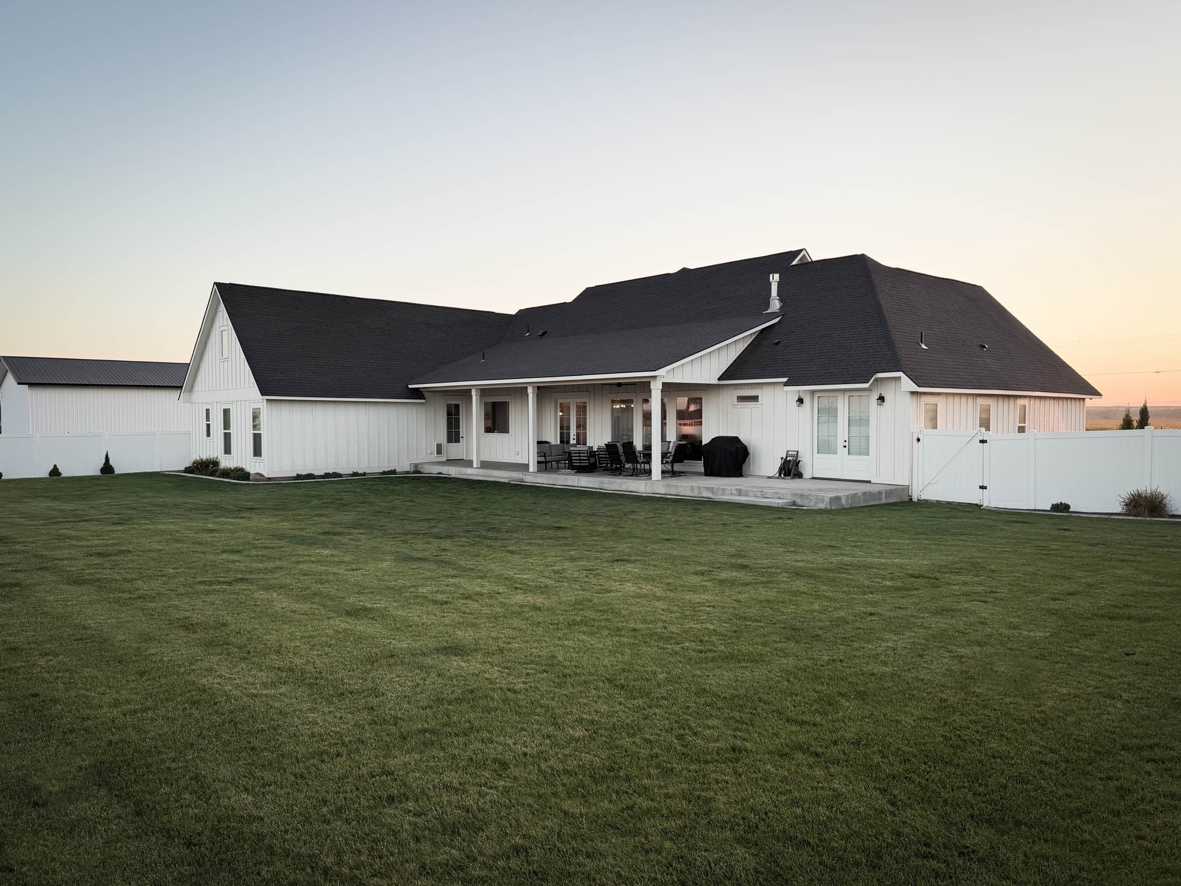 Backyard with covered patio and lush lawn at dusk
