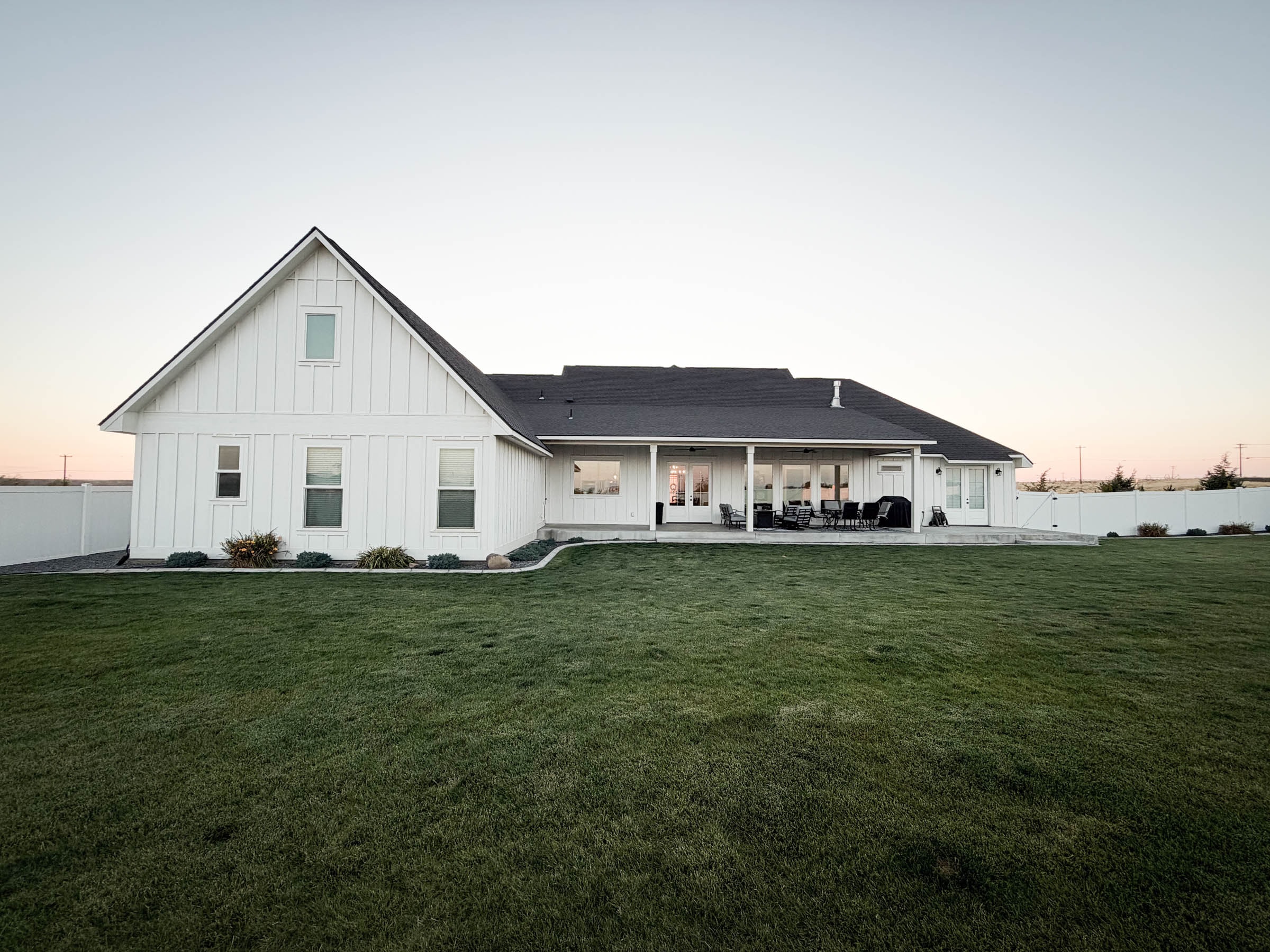 Backyard rear view with covered patio and open lawn at dusk