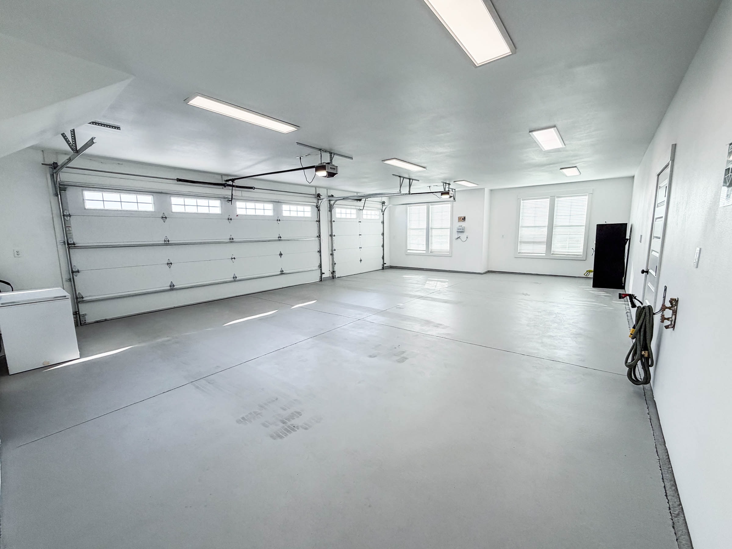 3-car garage interior with epoxy floor, two garage doors, and natural light