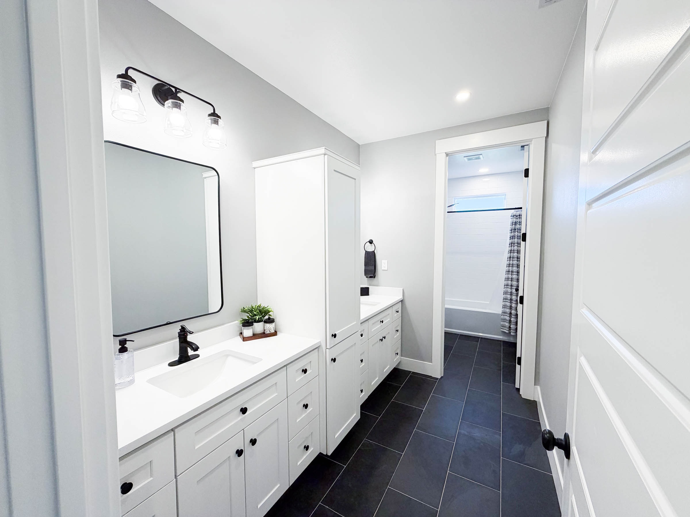 Bath 2 with double vanity, white shaker cabinets, black hardware, and dark tile floors