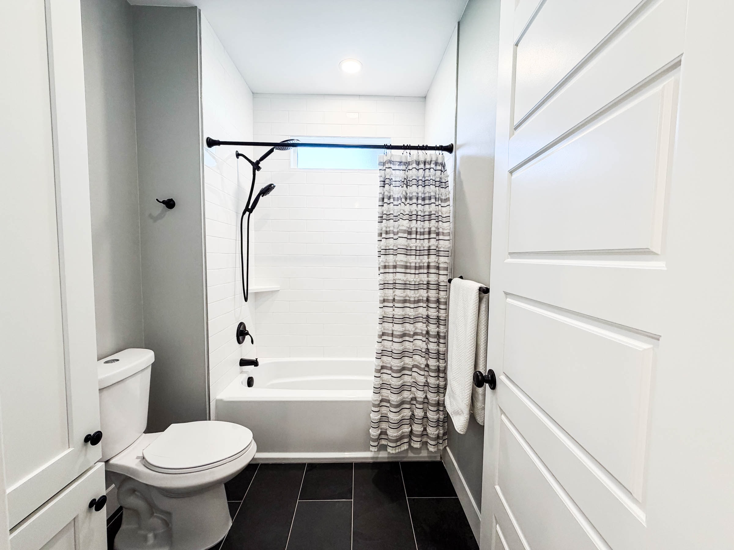 Bath 2 tub and shower with white subway tile, black fixtures, and dark tile floors