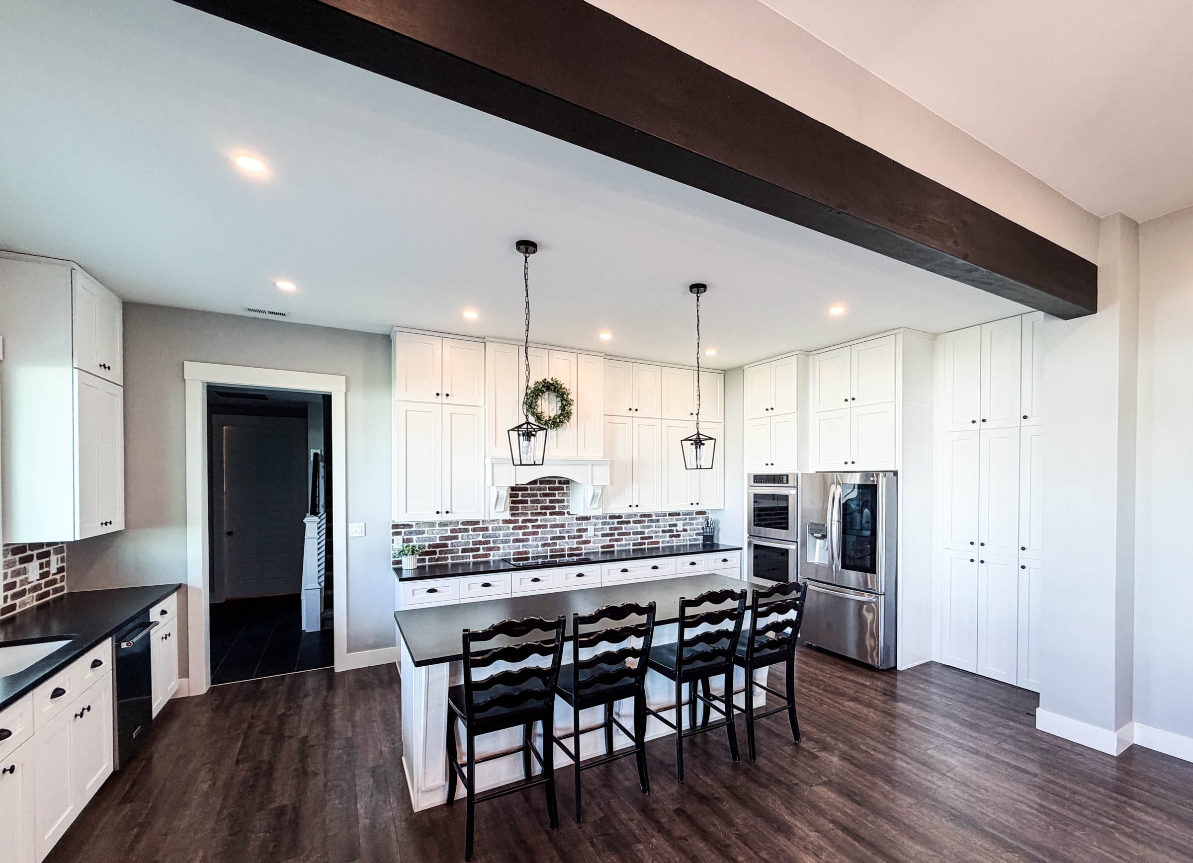 Kitchen with white cabinets, black island seating, brick backsplash, and dark wood beam