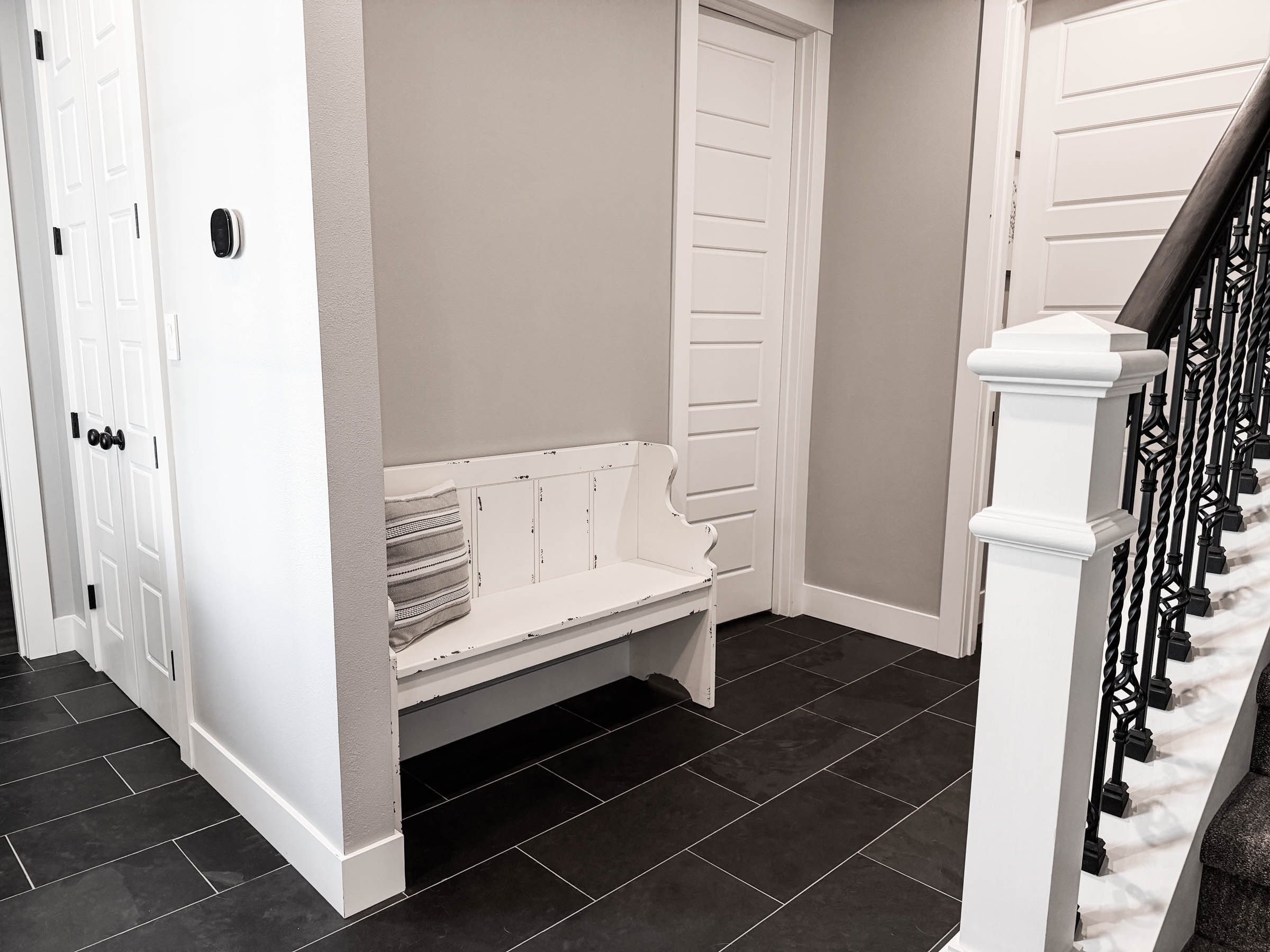 Mud room with bench, black tile floors, and staircase railing